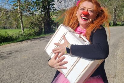 Una payasa abraza su maleta en una carretera de montaña.