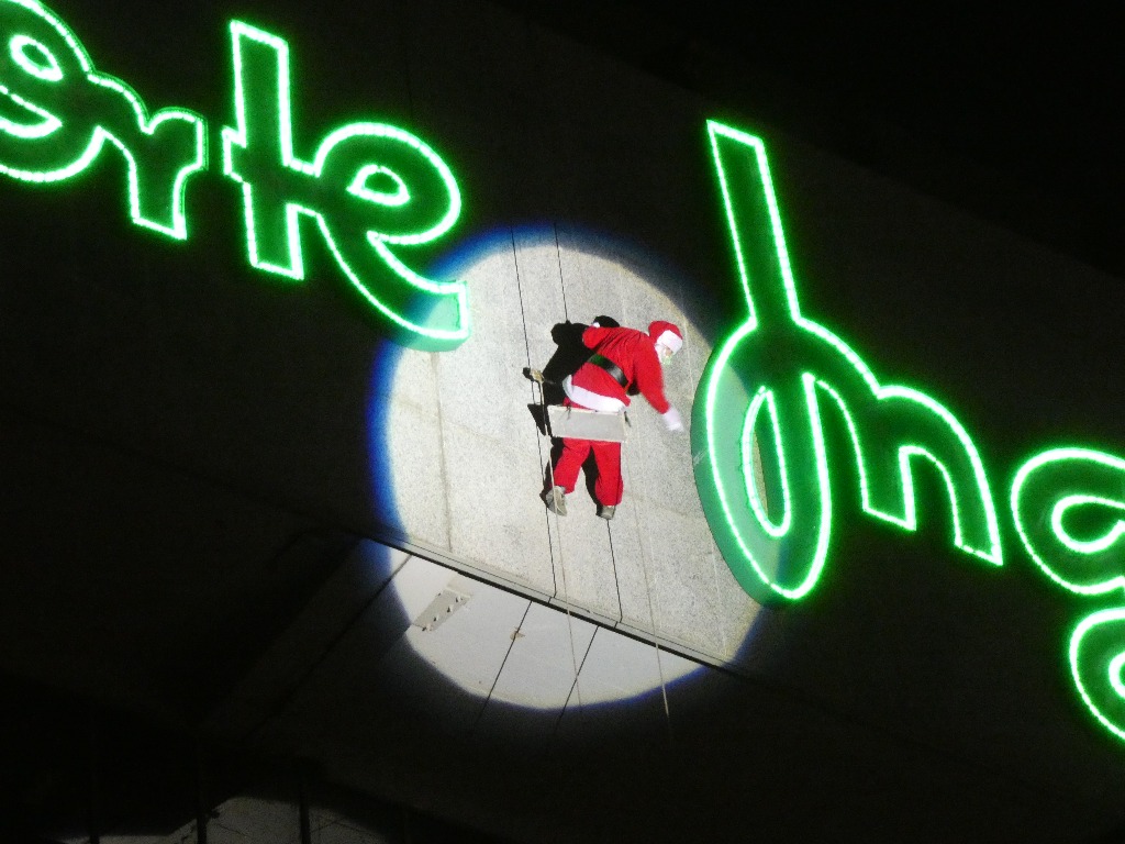 Papá Noel desciende colgado por la fachada de El corte Inglés de León iluminado por un foco