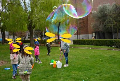 Niños y niñas juegan en un parque con grandes pompas de jabón