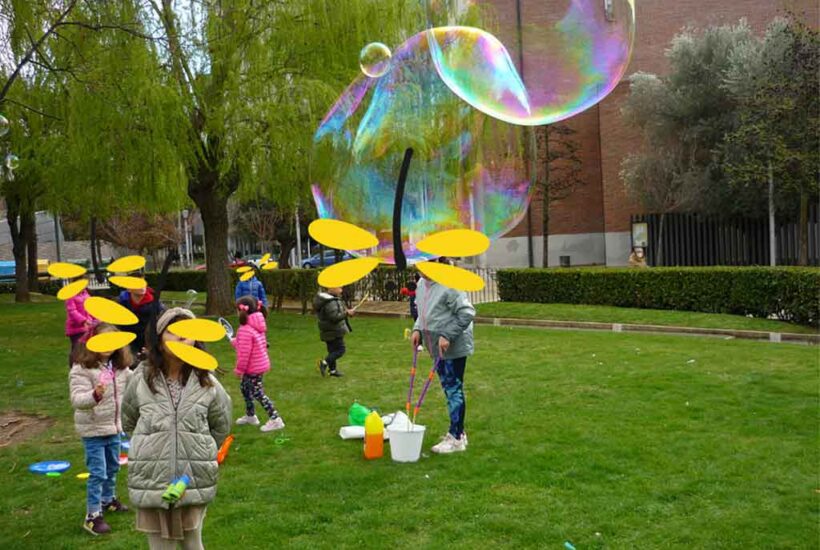 Niños y niñas juegan en un parque con grandes pompas de jabón