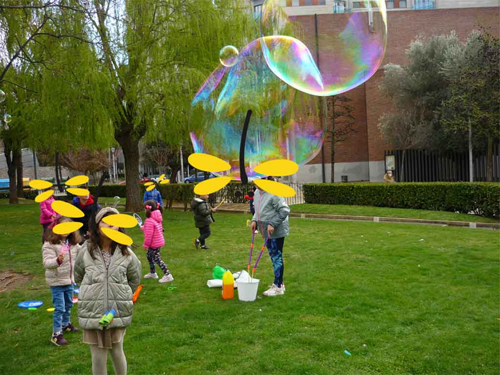 Niños y niñas juegan en un parque con grandes pompas de jabón