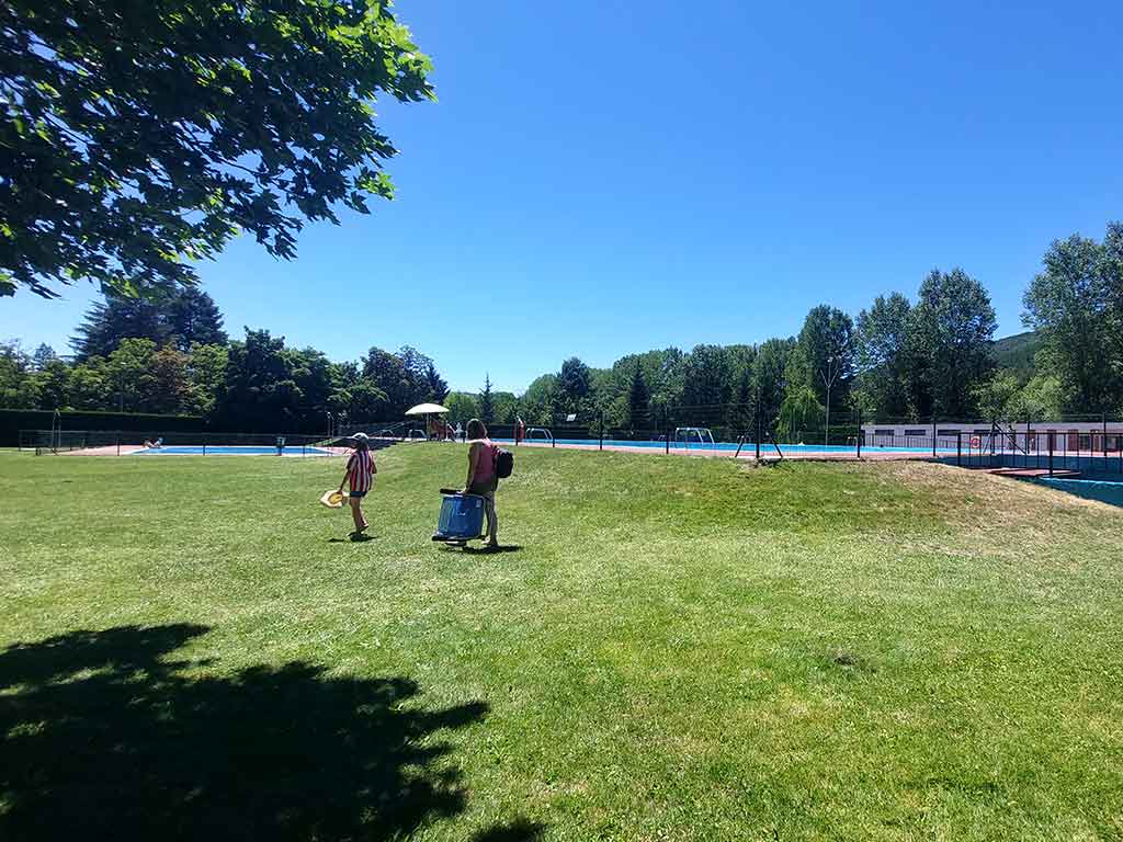 Dos personas llegan por la zona verde de las piscinas de Boñar