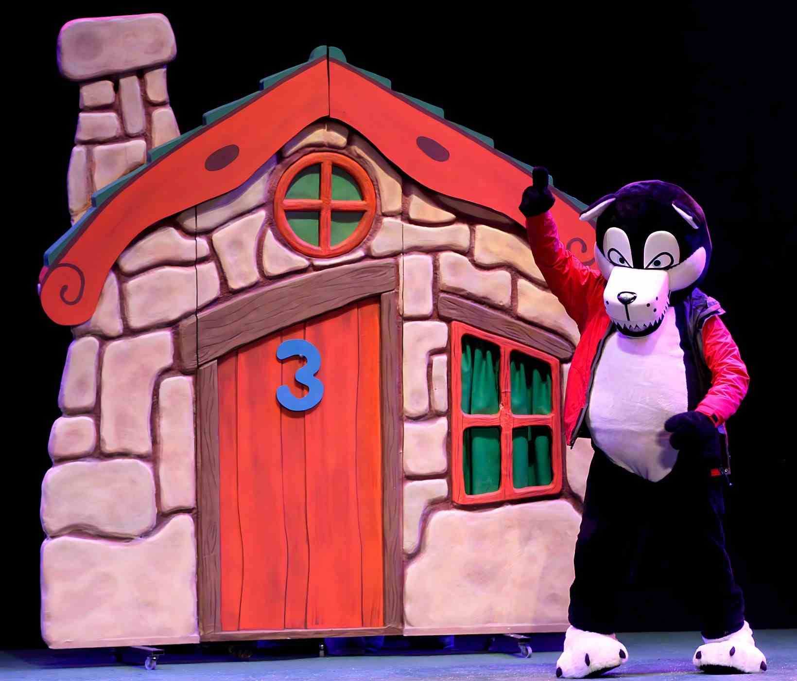 Personaje de Los tres cerditos junto a la casa de ladrillo.