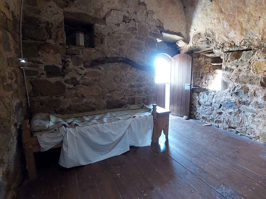 Una cama de madera en una habitación del castillo de Cornatel