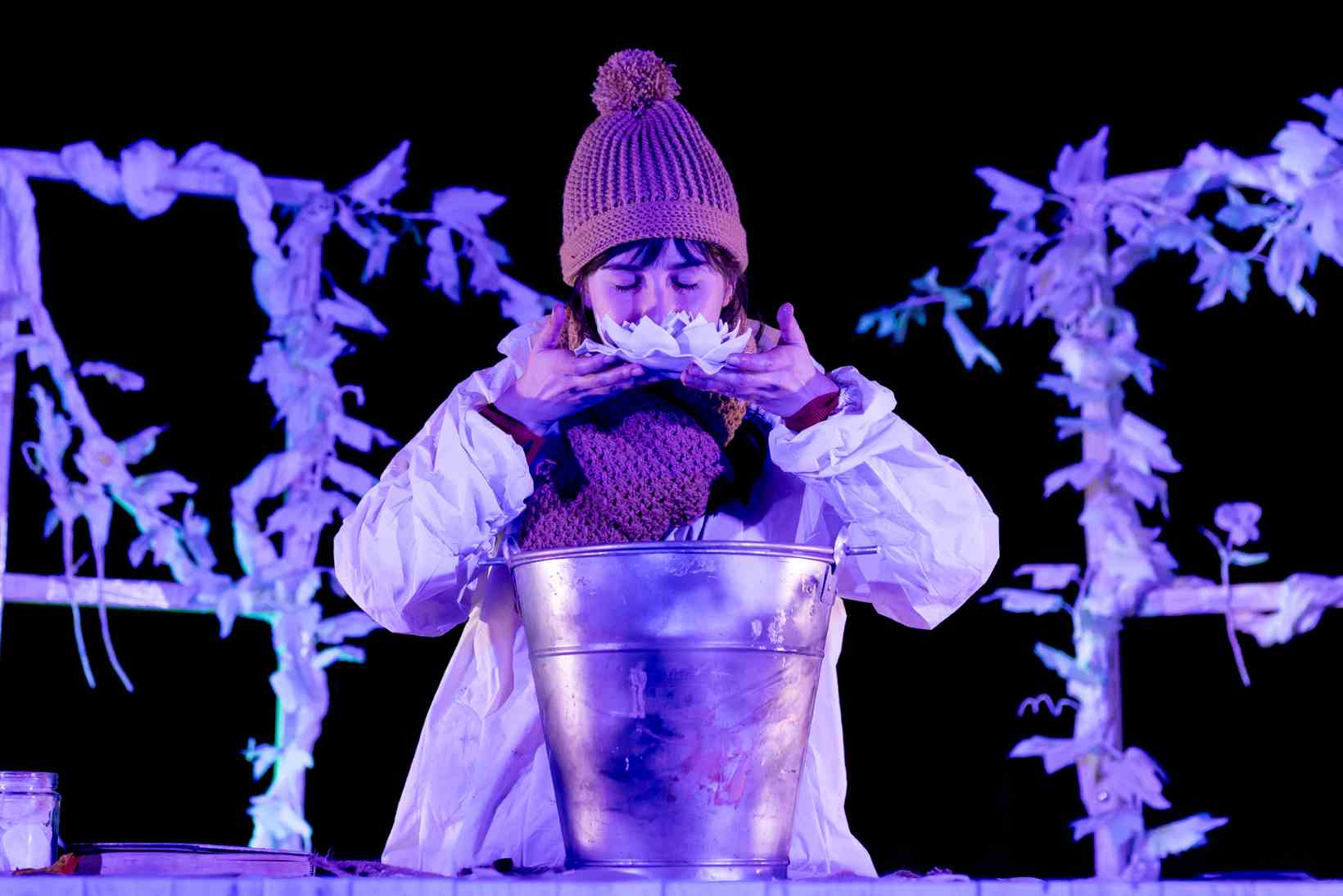 Una mujer huele unas plantas que sostiene con sus manos en un momento de la obra de teatro familiar El jardín de Olivia. 