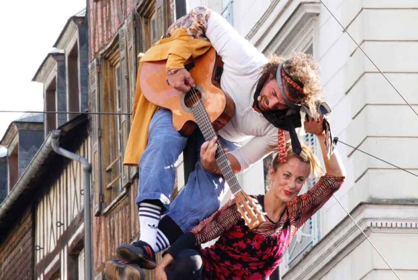 Un hombre toca la guitarra mientras hace equilibrismos junto a una mujer