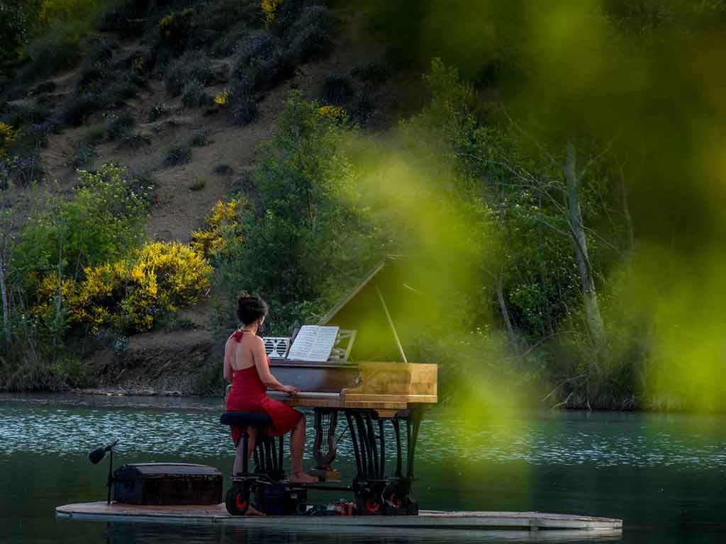 Una pianista toca el piano sobre una plataforma que flota en un lago. 
