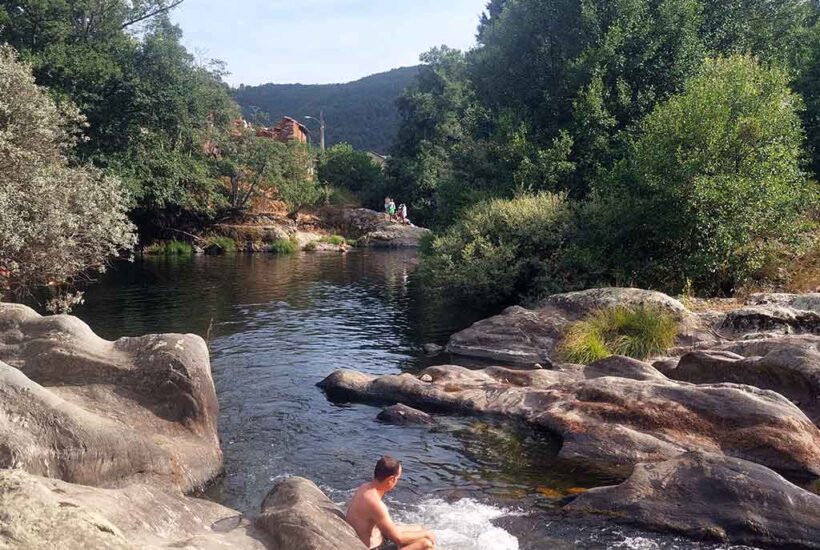 Un hombre descansa sobre una roca con los pies en el río a su paso por La Omañuela