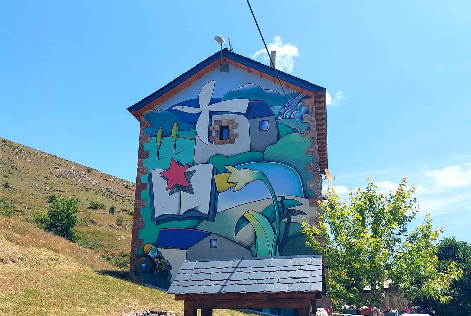 Colorido mural de Manolo sierra sobre la fachada de una casa en el pueblo de Lago de Babia