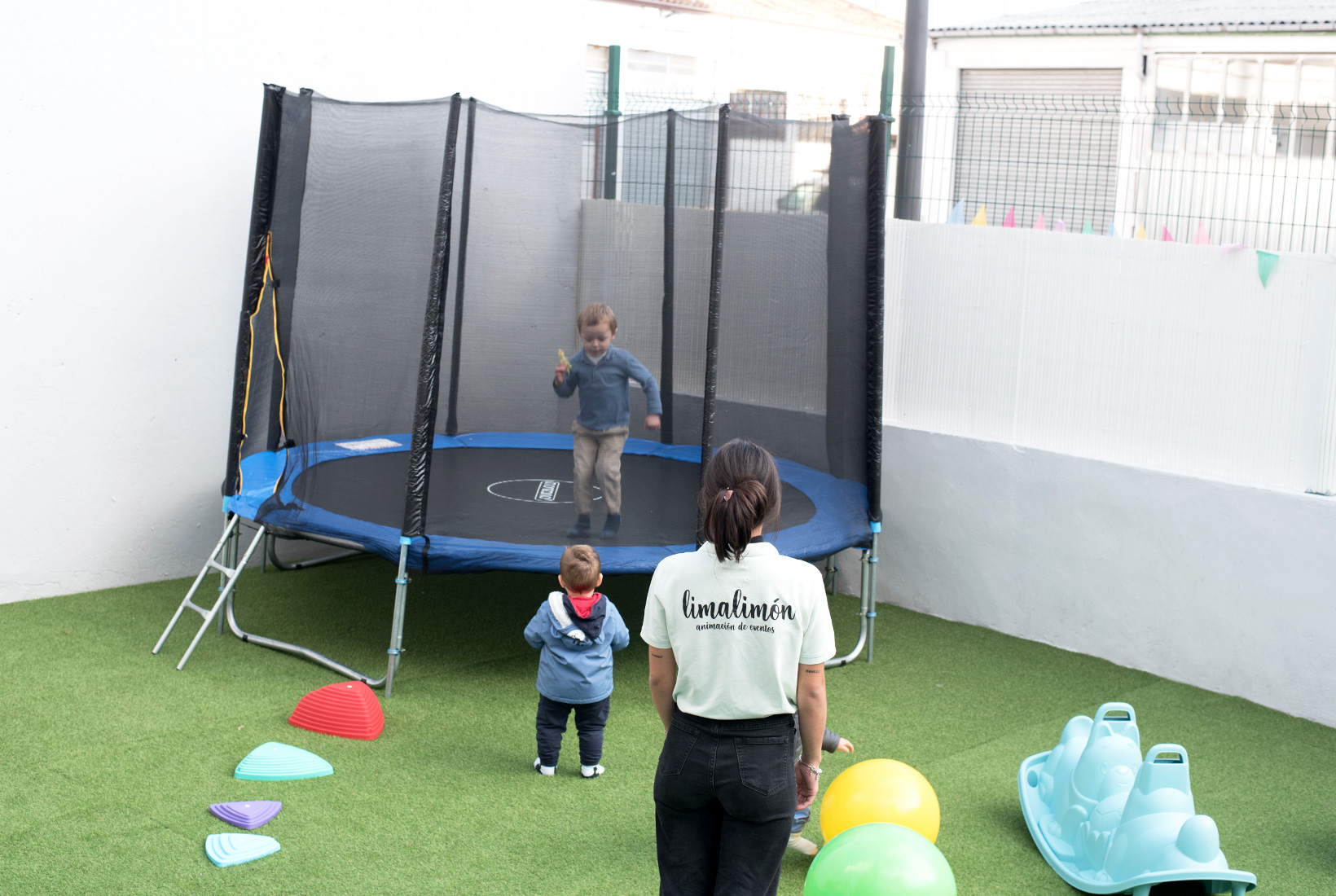 Dos niños juegan en el patio de Limalimón, cafetería para familias en León, bajo la atenta mirada de una monitora. Uno de los niños salta en el interior de una cama elástica.
