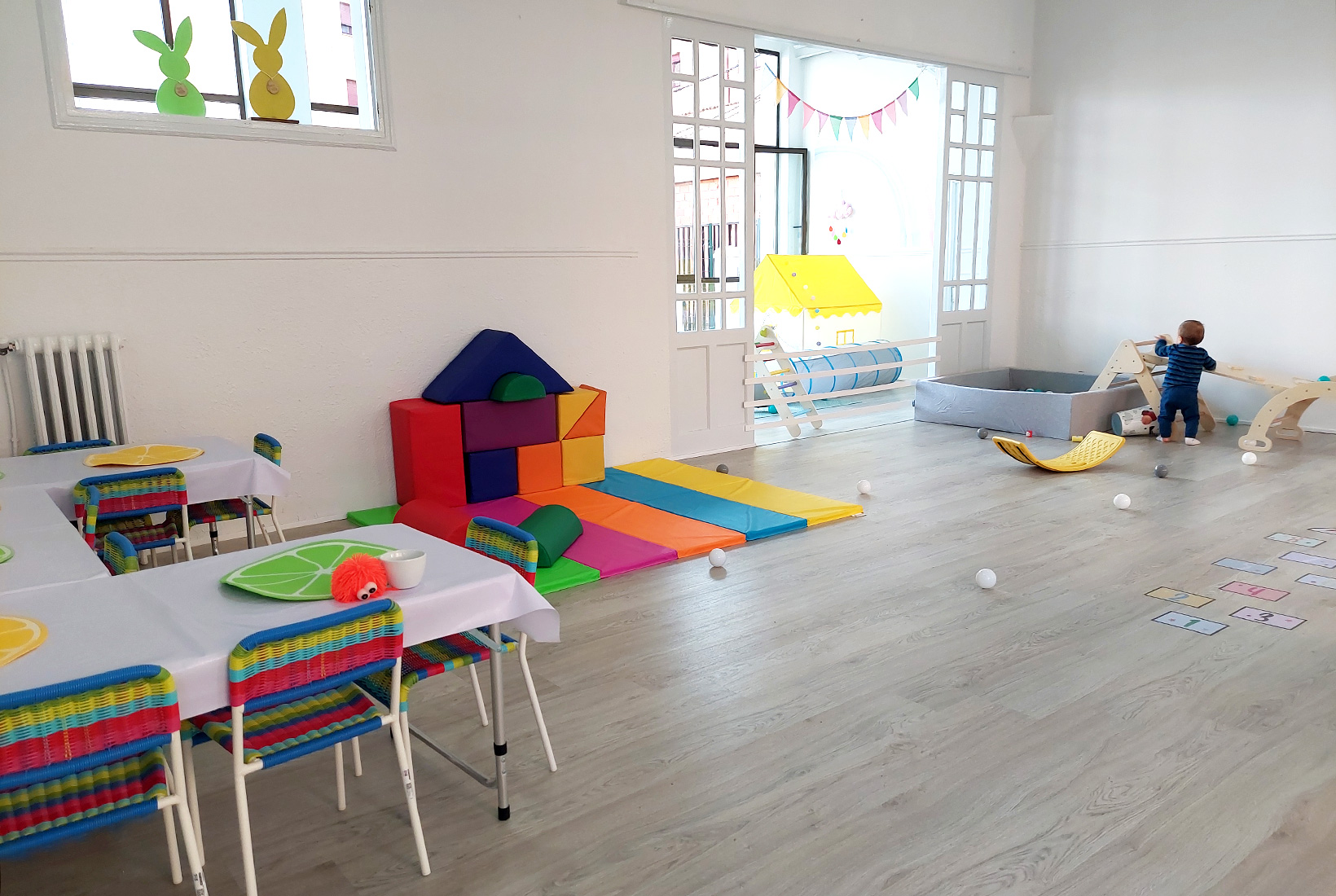 Sala infantil con mesas, sillas y juguetes donde juega un niño de 1 año en Limalimón, cafetería para familias en León.