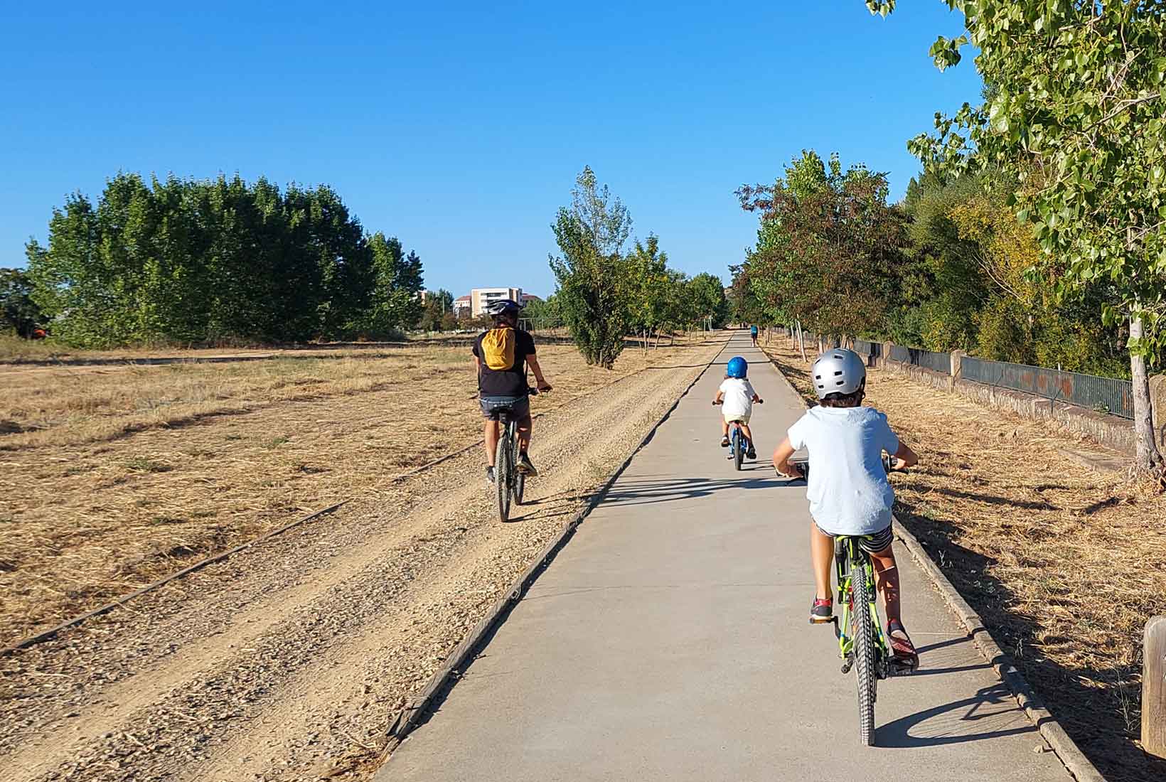 Un adulto y dos niños circulan en bicicleta por el carril bici de León junto al río. 