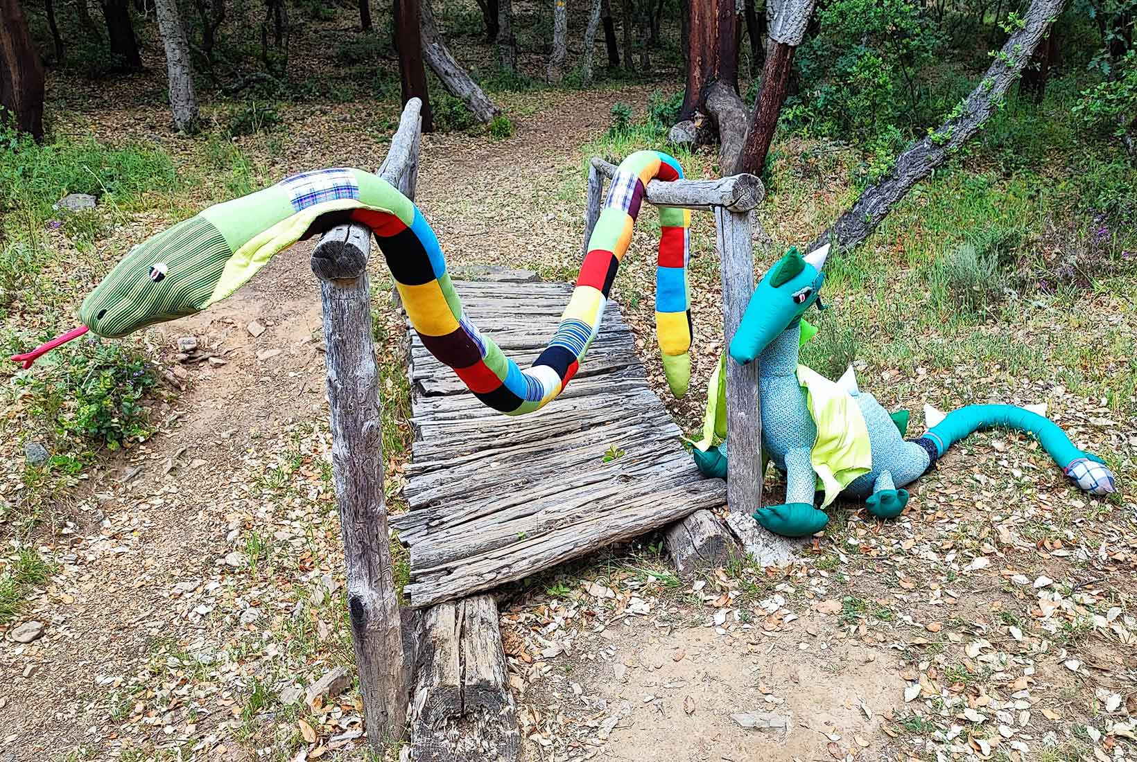 Una serpiente de peluche y un dragón junto a un pequeño puente en la Senda Encantada de Cobrana