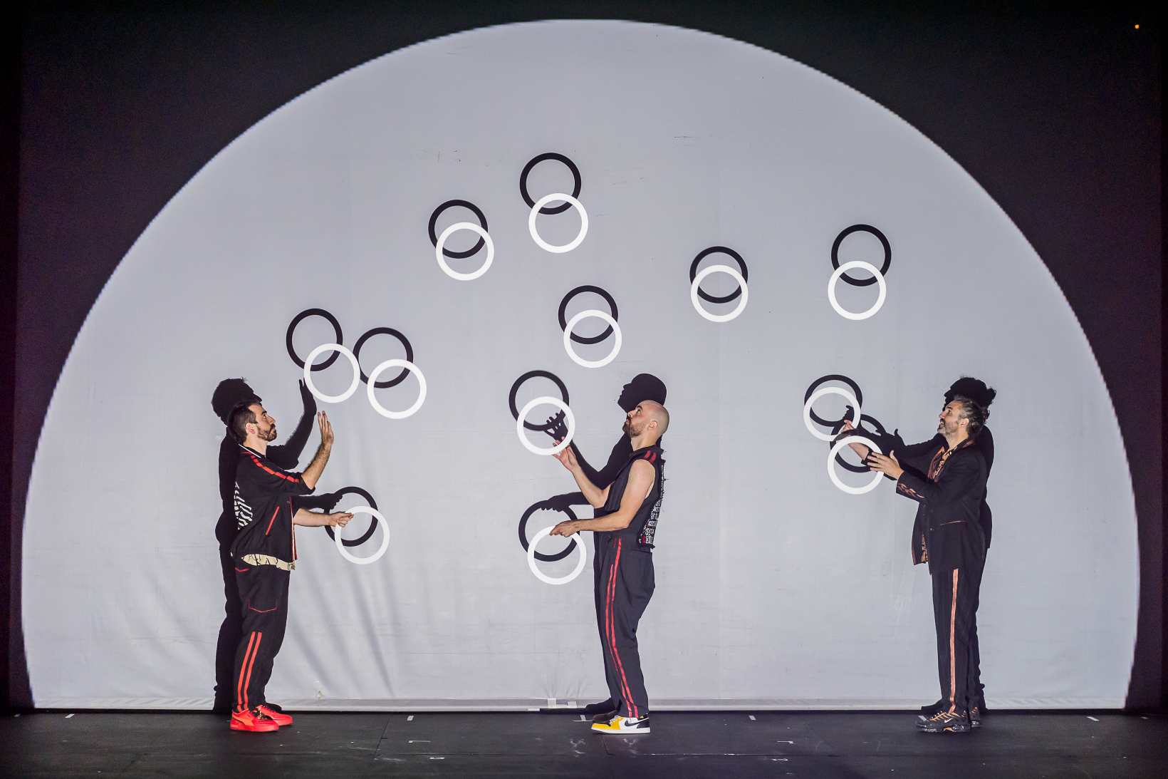 Tres hombres hacen malabares con anillas que lanzan hacia arriba en un momento de la obra de circo familiar Todo lo posible. 